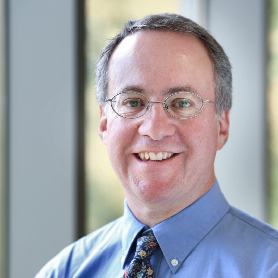 Dr. Alan Malter smiles at camera in glasses and blue button up shirt.